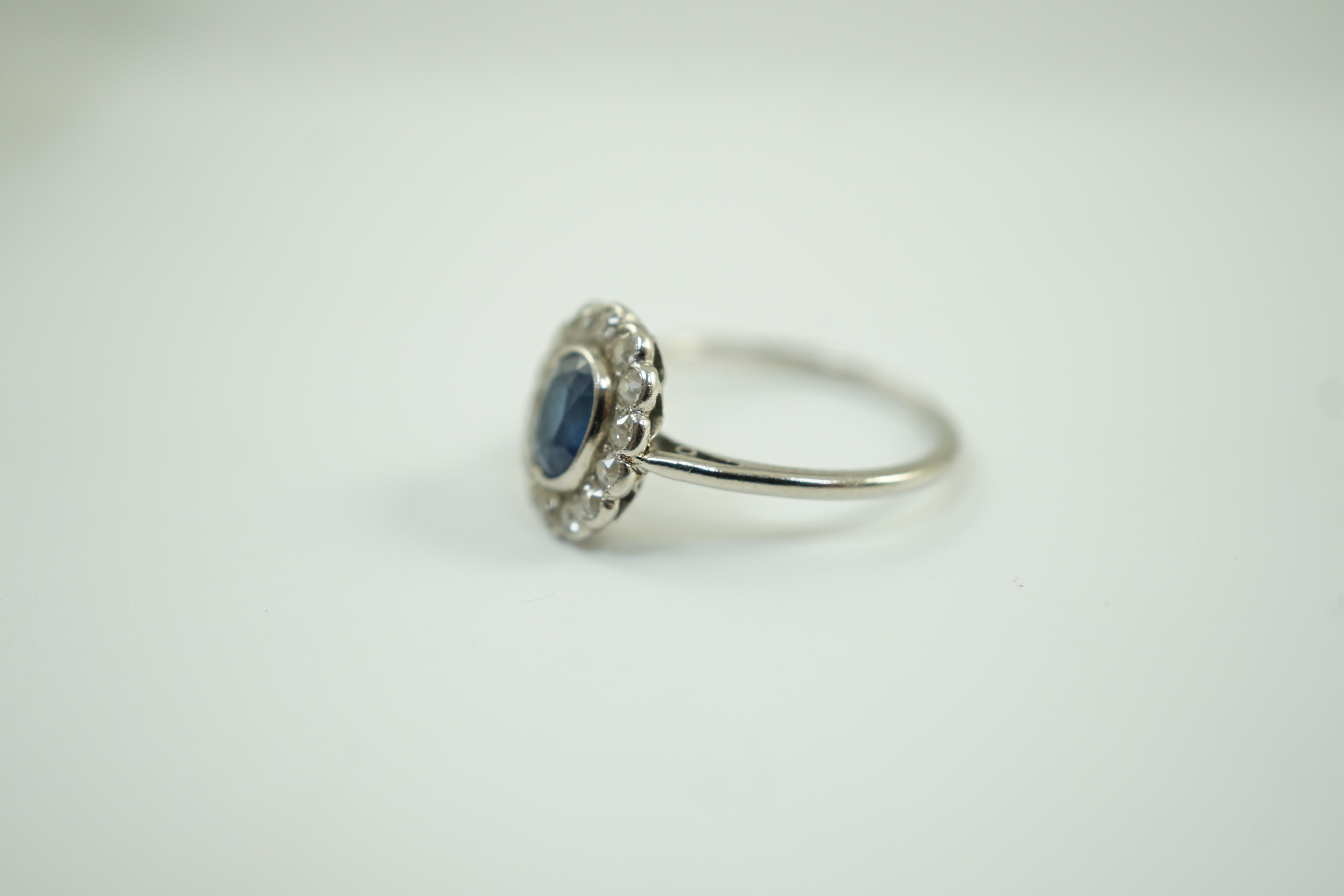 A white metal, sapphire and diamond set oval cluster ring, size M/N, gross weight 2 grams.